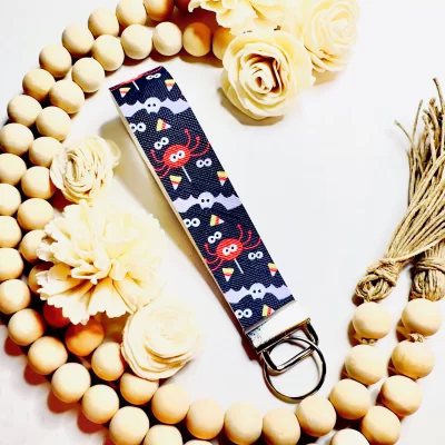 This photo shows an orange spider faux leather key fob with silver hardware. Other items in the image include wood beads and natural colored wood flowers.